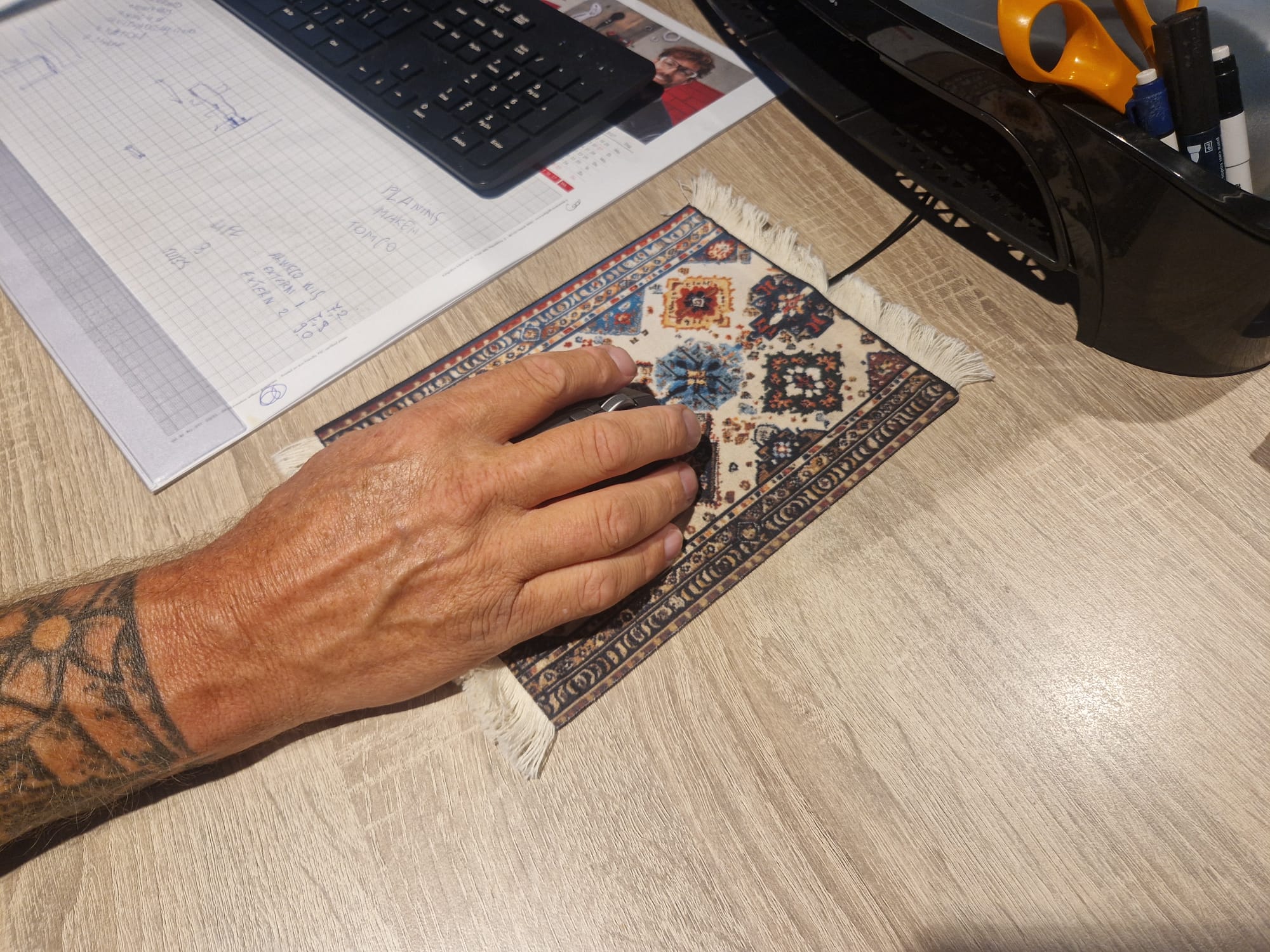 Hand op de muis boven de verwarmde muismat met Perzisch dessin op een kantoorbureau